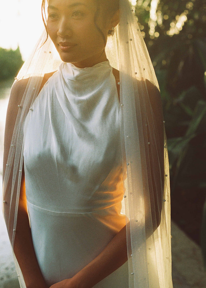 Bride wearing a wedding dress with a pearl veil, single tier, cathedral length in an outdoor setting