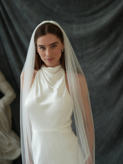 Front view of a woman wearing a white wedding dress with a simple plain classic veil, cathedral length, single tier