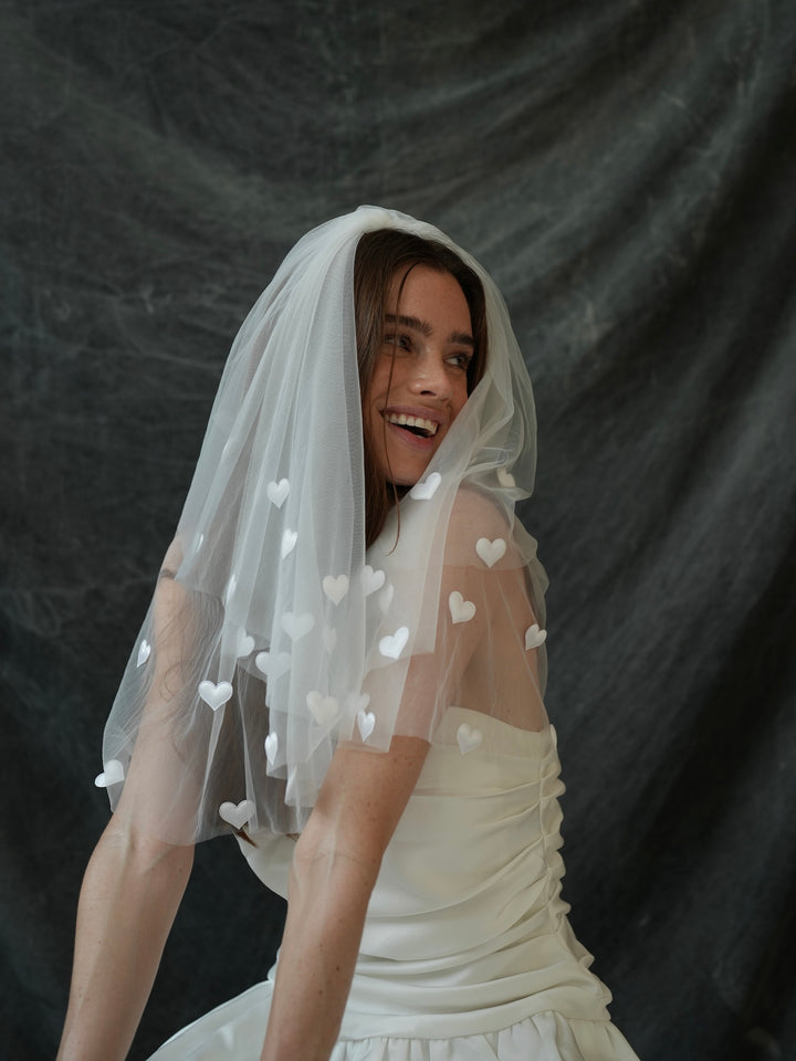 Woman wearing a white wedding dress with a mini bachelorette veil featuring heart patterns