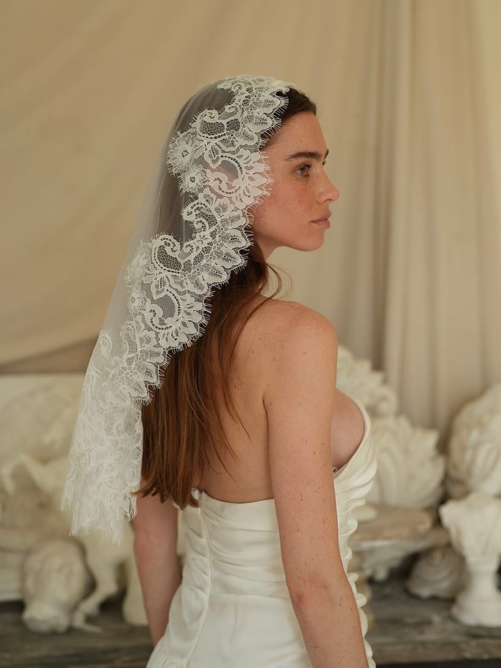 Woman wearing a mini mantilla short lace bachelorette veil in an elegant indoor setting