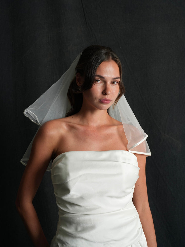 Woman wearing a mini satin short two tier bachelorette veil against a dark background