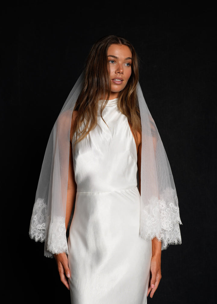Woman wearing a white wedding dress with a short lace veil fingertip length
