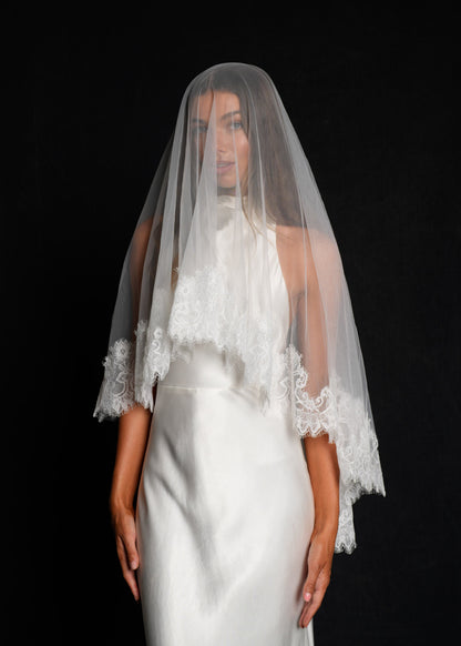 Woman wearing a white wedding dress with a short lace veil, two tier, fingertip length draped over her face