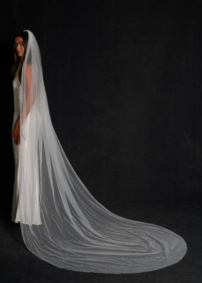 Woman wearing a cathedral length, elegant pearl veil against a black background