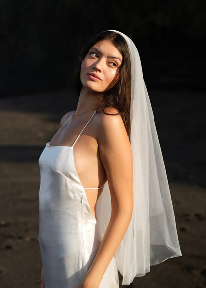 Woman in a white dress showing a side angle of a short simple plain classic veil on a beach