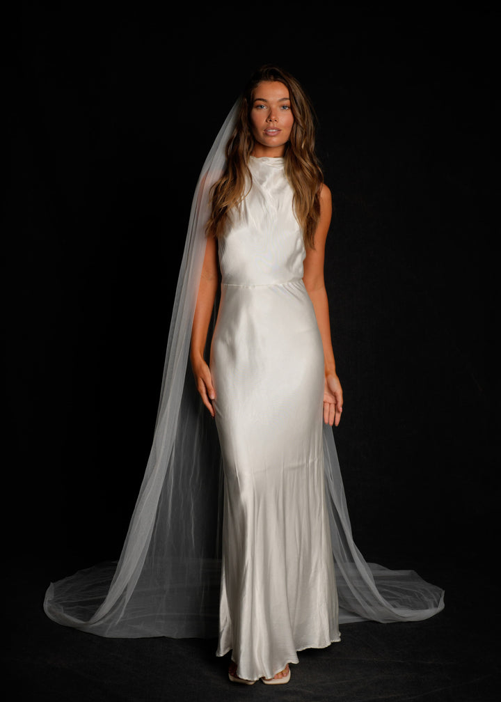 Woman wearing a white wedding dress with a simple plain classic veil, cathedral length, single tier on a black background