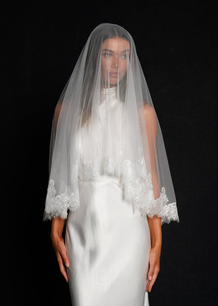 Bride wearing a white wedding dress with a chantilly short lace veil, two tier, fingertip length draped over her face