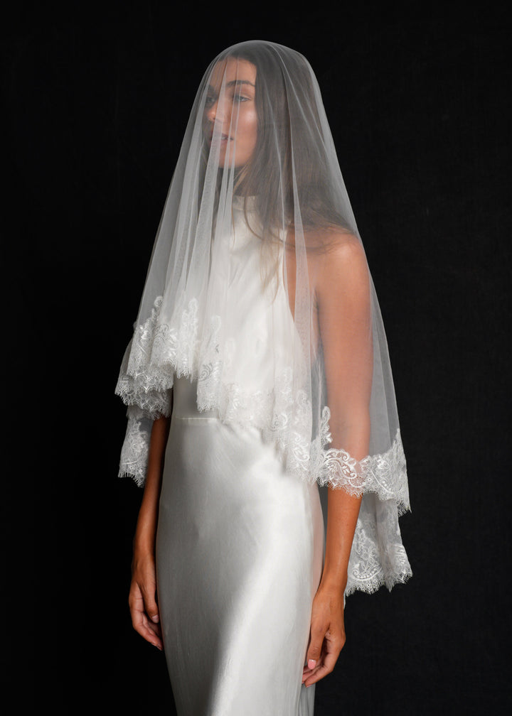 Bride in a white gown wearing a chantilly short lace veil, two tier, fingertip length shown in full coverage