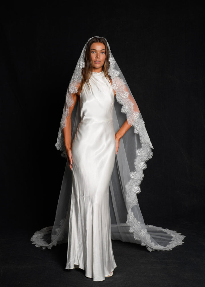 Woman wearing a white wedding dress with a mantilla chantilly lace veil, single tier, cathedral length on a black background