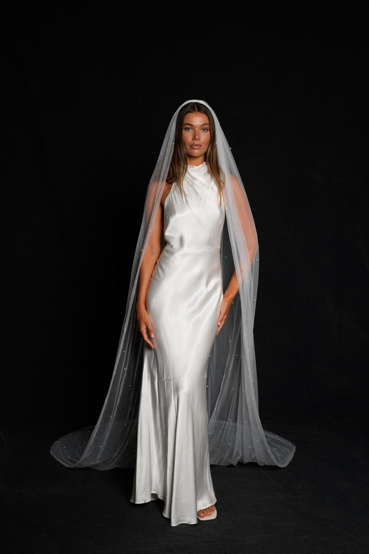 Woman wearing a white wedding dress with a cathedral length, single tier, pearl veil
