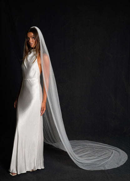 Woman wearing a white wedding dress with a cathedral length pearl veil in full coverage