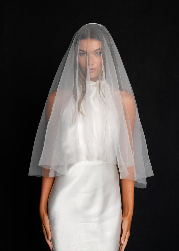 Woman wearing a white wedding dress with a short simple plain classic veil, fingertip length, two tier draped over her face